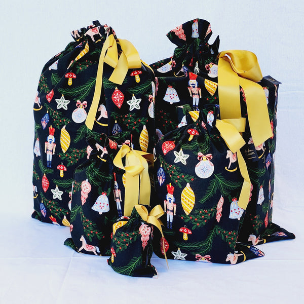 Set of five reusable Christmas gift bags in Ornament. Bags are black with colourful Christmas ornaments hanging off Christmas branches. Bags are tied with yellow satin ribbon.