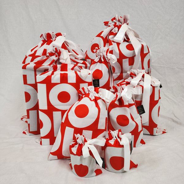A photo showing a sewn up set of Sew Your Own Gift Bags in HOHOHO. The fabric is red with white letters spelling HOHOHO, and the bags are tied with a white satin ribbon.