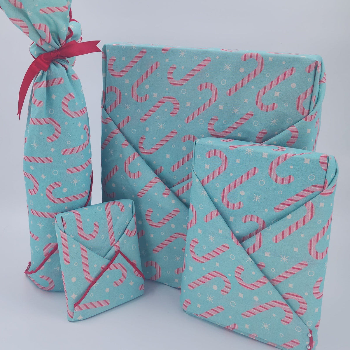 Furoshiki cotton gift wrap on on four gifts in turquoise background with red and pink candy canes.