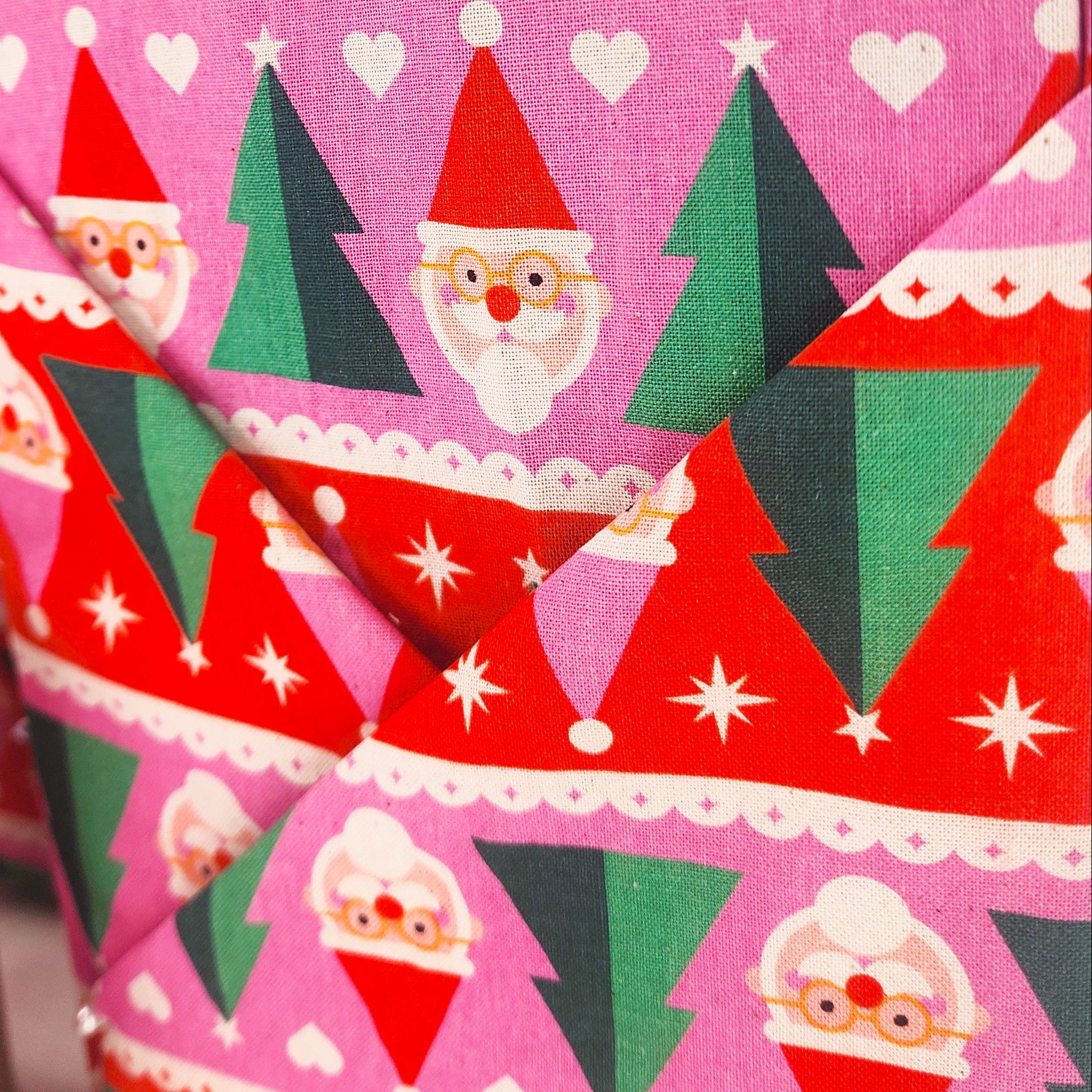 Close-up of Christmas-themed cotton gift warp with a repeating pattern of Santa Claus faces, green Christmas trees, and white hearts on pink and red backgrounds.