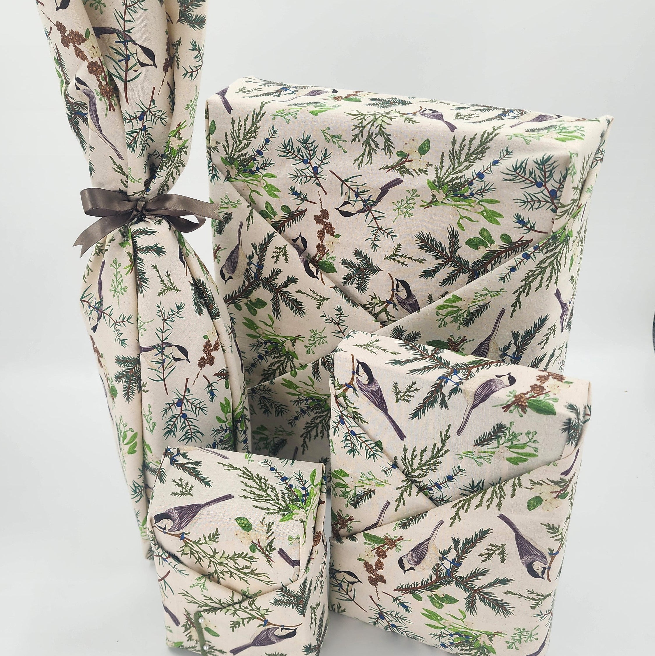 Furoshiki cotton gift wrap on on four gifts in natural cotton with green boughs and seeds, with grey birds and flora design