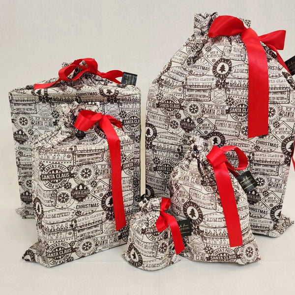 Set of five reusable Christmas gift bags in Santas Mail. Bags are white with black Christmas postage stamps on them, tied with a red satin ribbon.