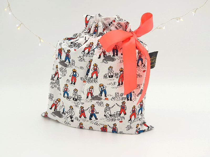 Small Hard Hats Required reusable gift bag. Fabric has drawing of men at work wearing hard hats, on a white background. Bag is tied with orange ribbon.