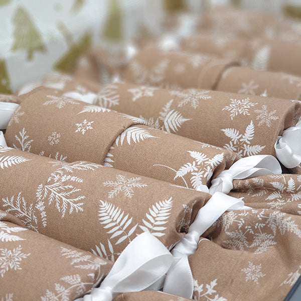 Close up photo of Snowflake Sew Your Own Re-Crackers (reusable Christmas crackers or bon bons) once they have been made up. The fabric has white silver fern snowflakes, and they are fastened with white satin ribbon.
