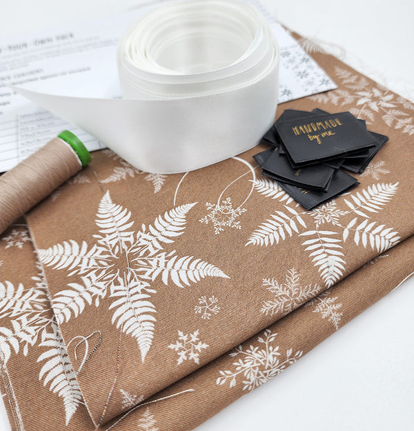 Photo showing contents of the set of ten Sew Your Own Gift bags in Snowflake. There is fabric, thread, ribbon, instructions and tags. The snowflake fabric is a natural colour with a white silver fern snowflake.