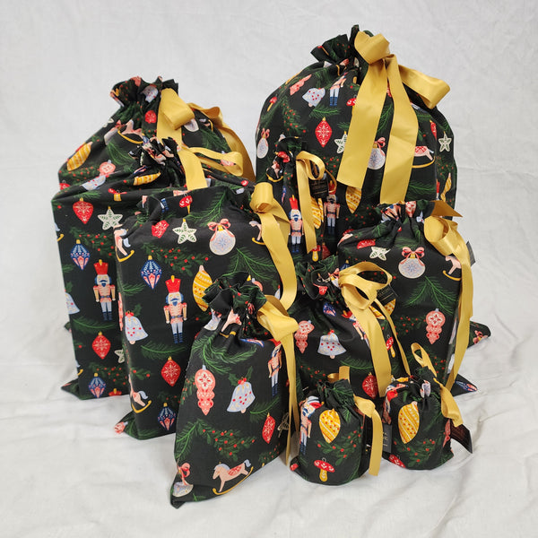 A photo showing the set of Sew Your Own Gift Bags in Ornament all sewn up. The fabric is black with colourful Christmas ornaments hanging off tree branches and the bags are tied with gold satin ribbon.