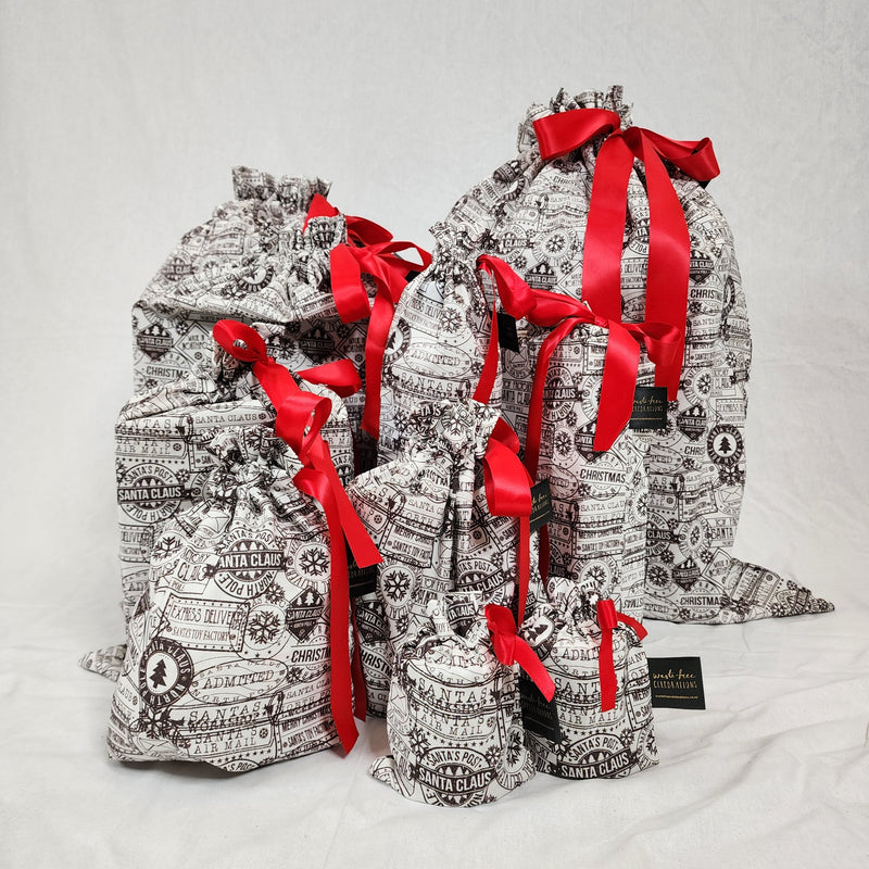 A photo showing a sewn up set of the Sew Your Own Gift Bag in Santas Mail. The fabric is white with black postage stamps on it, and the bags are tied with red satin ribbon.