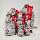 Set of ten reusable Christmas gift bags in Santas Mail. Bags are white with black Christmas postage stamps on them, tied with a red satin ribbon.
