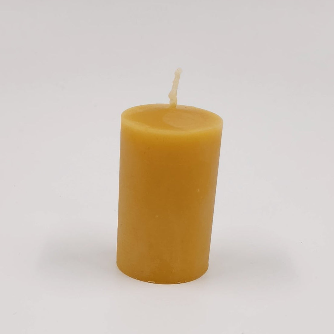 A single small cylindrical candle in a warm golden-yellow color, standing upright on a plain light gray studio background.