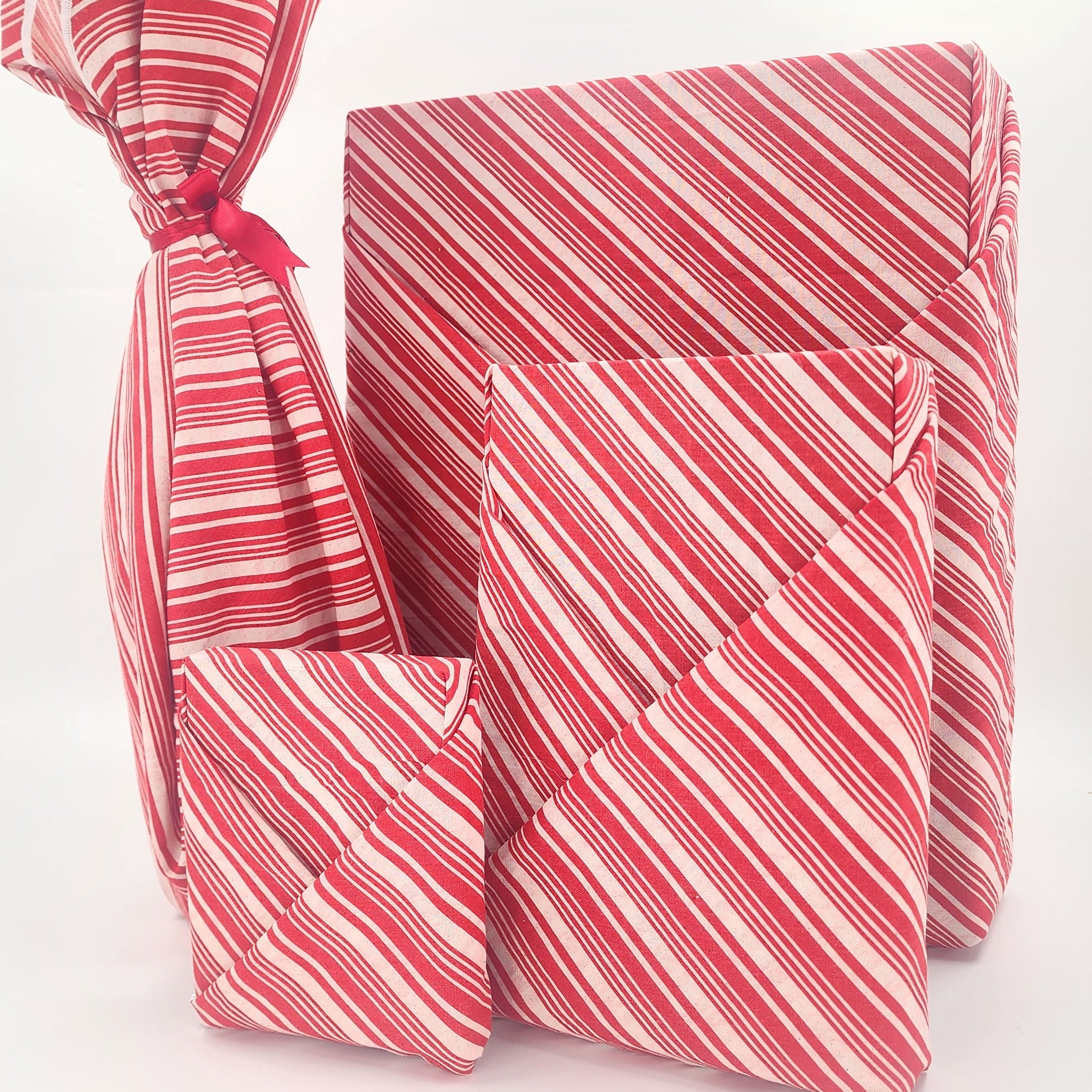 four fabric wrapped parcels in a red and white striped candy cane pattern, arranged on a plain white studio background.