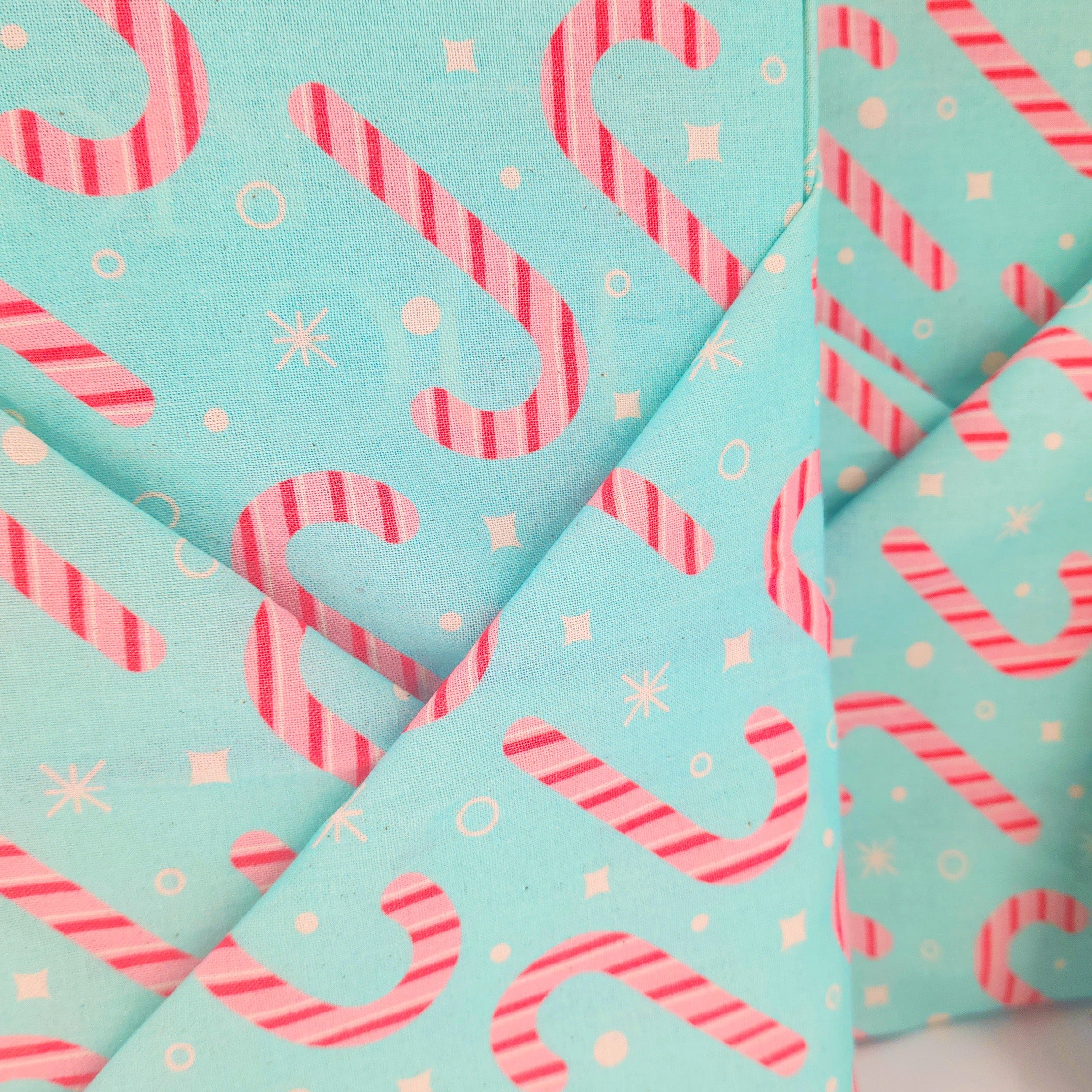 A close-up of folded furoshikiwith a mint green background and a repeating pattern of pink-and-white striped candy canes, small white stars, and white snowflake-like motifs.