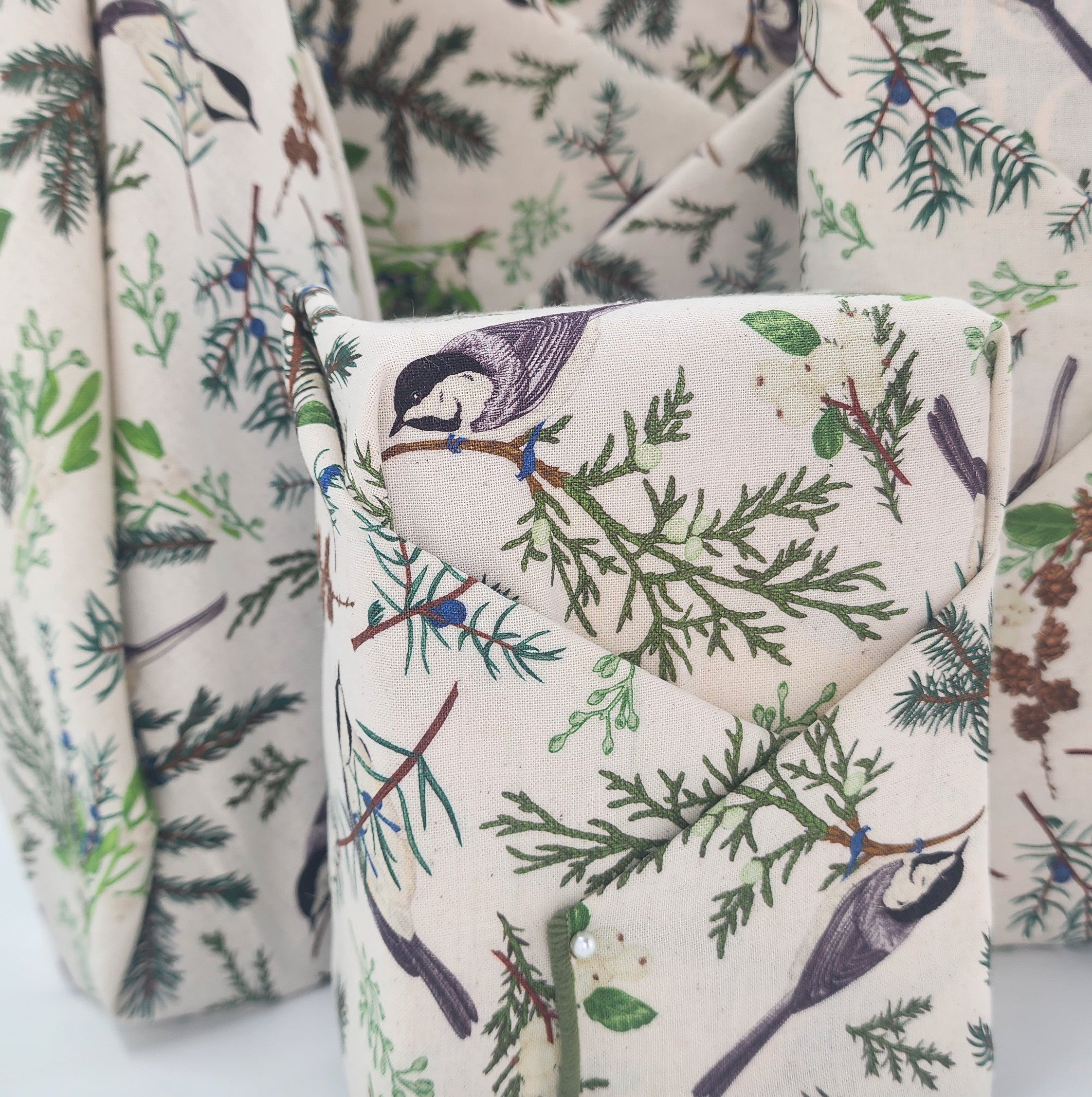 Furoshiki cotton gift wrap on on four gifts in natural cotton with green boughs and seeds, with grey birds and flora design