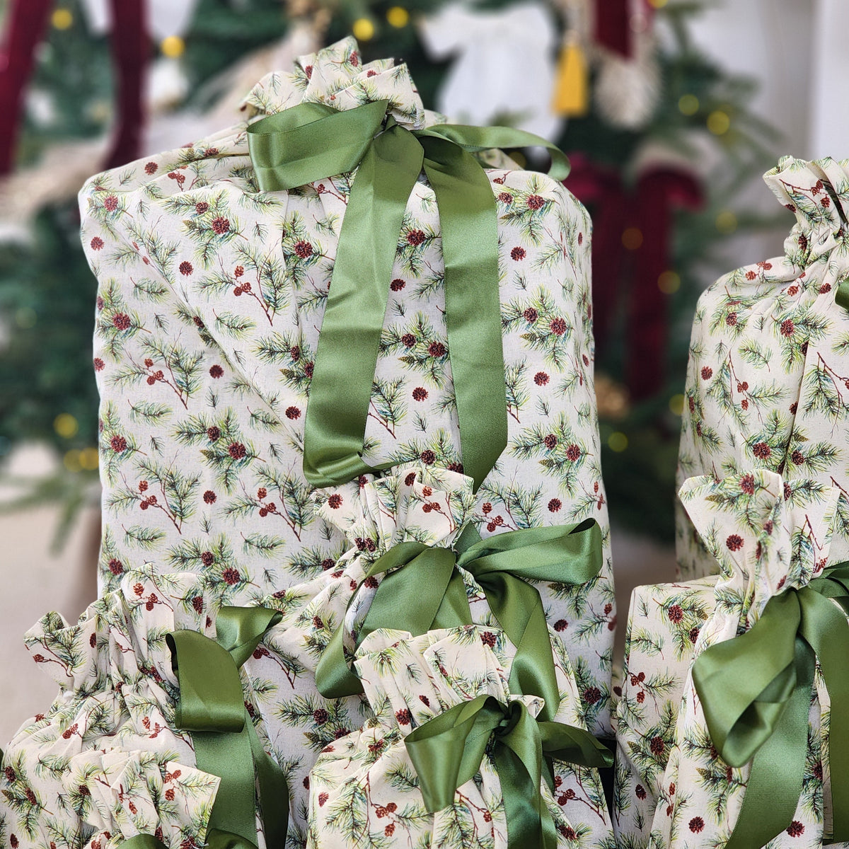 A stack of Christmas wrapped gifts in matching holiday-themed cotton wrapping with a green pine and holly berry print, tied with olive green satin ribbons.