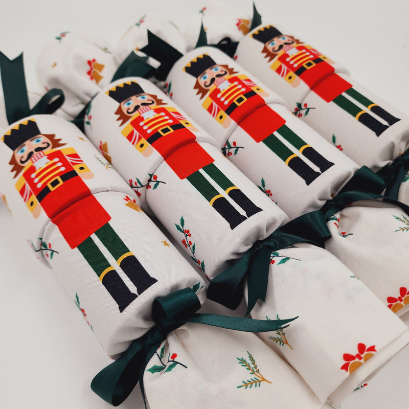 Set of four Re-Crackers (reusable Christmas Crackers or bon bons) featuring a large nutcracker figure on white fabric. Finished with green satin ribbon.