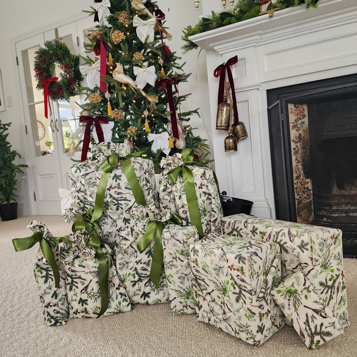 A collection of Christmas wrapped gifts in a matching green and white holly patterned cotton, arranged around a decorated Christmas tree in a living room setting.