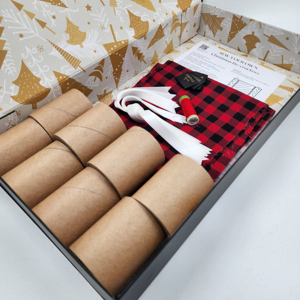 Photo showing contents of a Sew Your Own Re-Cracker (reusable Christmas crackers or bon bons) box. The fabric is American Plaid - a black and red check, and there is ribbons, tags, instructions, cardboard tubes and thread.