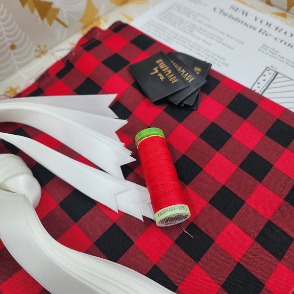 Closeup photo of American Plaid fabric, with instructions, tags and thread. The fabric is red and black check.