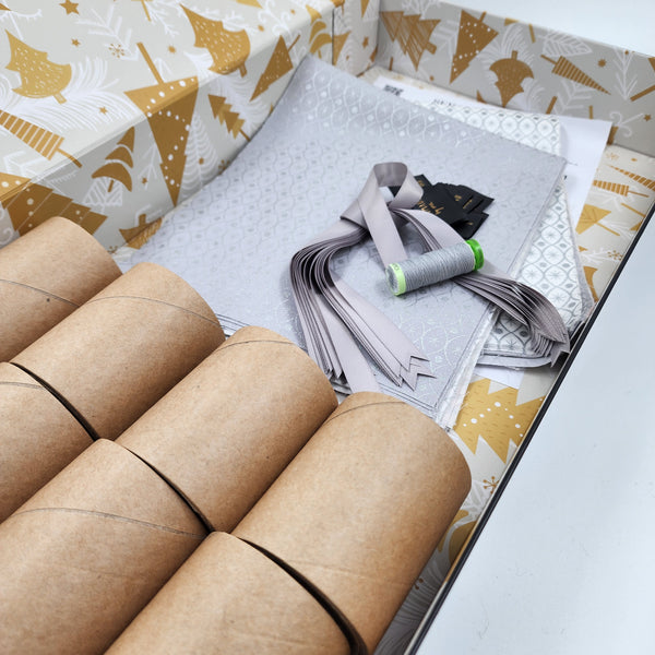 Photo showing contents of a Silver and Ice Sew Your Own Re-Cracker (reusable Christmas crackers or bon bons) box.  There is silver ribbon, tags, fabric, instructions, cardboard tubes and thread. The fabric is silver and white with a metallic silver print.