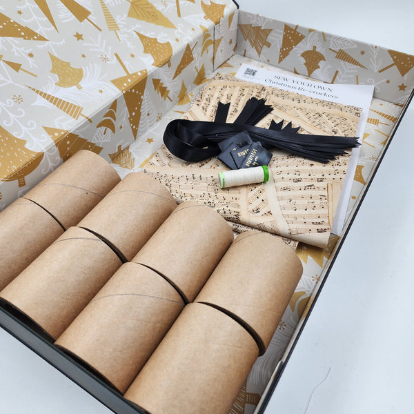 Photo showing contents of a Beethoven and Bronte Sew Your Own Re-Cracker (reusable Christmas crackers or bon bons) box. The fabric is has images of old sheet music on it, there is black satin ribbon, instructions, cardboard tubes, tags and thread.