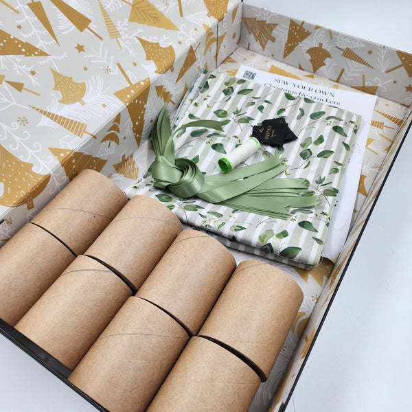 Photo showing contents of a Australiana Watercolour Sew Your Own Re-Cracker (reusable Christmas crackers or bon bons) box. The fabric has taupe and white stripes with green leaves, there is ribbons, instructions, cardboard tubes tags and thread.