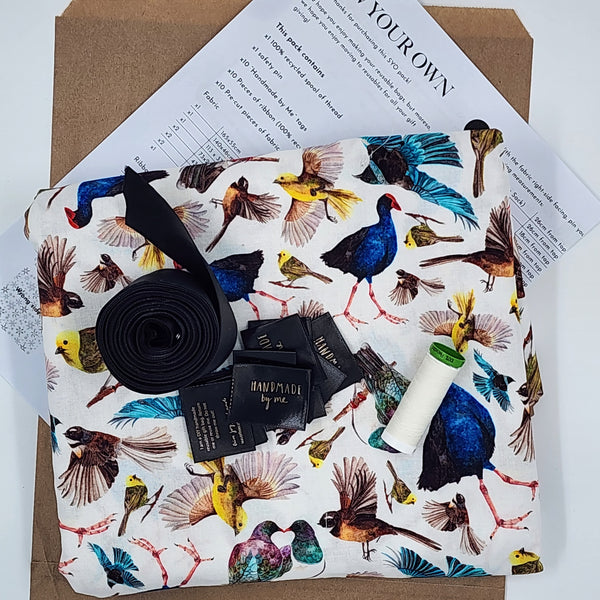 A photo showing the contents of a Sew Your Own Gift Bag set in NZ Birds. There is fabric, instructions, satin ribbon, thread and tags. The fabric features native NZ birds on a white background.