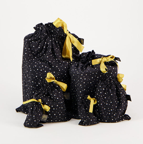 Photo shows a set of five Black Starry Night Reusable Gift Bags. Fabric is black with white tiny stars, bags are tied with gold satin ribbons.