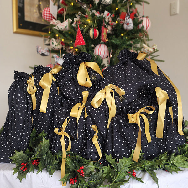 Photo shows a set of ten Black Starry Night Reusable Gift Bags. Fabric is black with white tiny stars, bags are tied with gold satin ribbons.