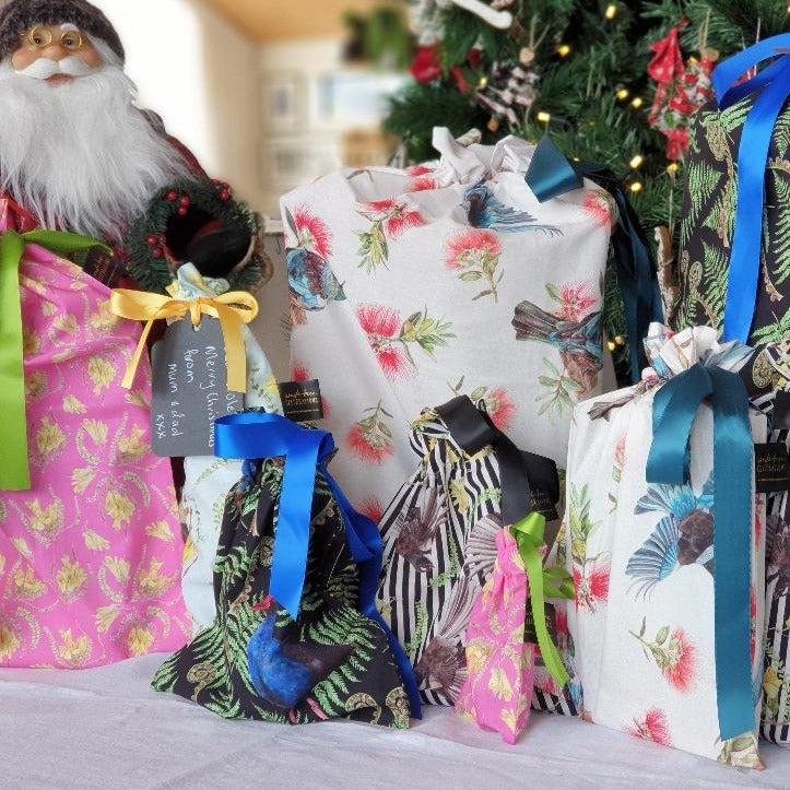 Photo shows a selection of Mixed Kiwiana reusable gift bags filled and under the tree.
