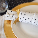 Close up of white Starry Night Re-Crackers (reusable Christmas Crackers or Bon bons). the cracker is white with tiny black stars and is finished with a gold ribbon. The cracker is sitting on a plate.