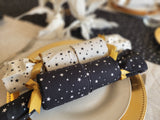 Close up of two Starry Night Re-Crackers (reusable Christmas Crackers or Bon bons). One cracker is white with tiny black stars, and the other is black with tiny white stars. They are finished with a gold satin ribbon. They are sitting on a plate.
