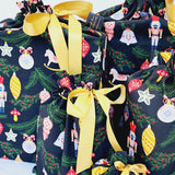 Close up of Ornament reusable Christmas gift bags. Bags are black with colourful Christmas ornaments hanging off Christmas branches. Bags are tied with yellow satin ribbon.