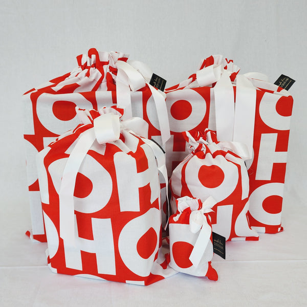 Set of five reusable Christmas gift bags in HOHOHO. Bags are red with the words HOHOHO in large white lettering. Bags are tied with a white satin ribbon.