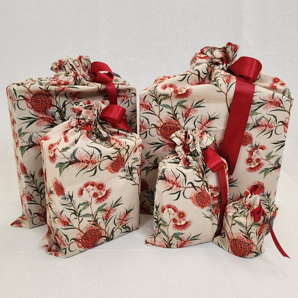 Set of five reusable Christmas gift bags in Australiana Eucalyptus. Fabric has red and green eucalyptus flowers on a natural coloured background. The bags are tied with a red satin ribbon.