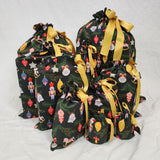 Set of ten reusable Christmas gift bags in Ornament. Bags are black with colourful Christmas ornaments hanging off Christmas branches. Bags are tied with yellow satin ribbon.
