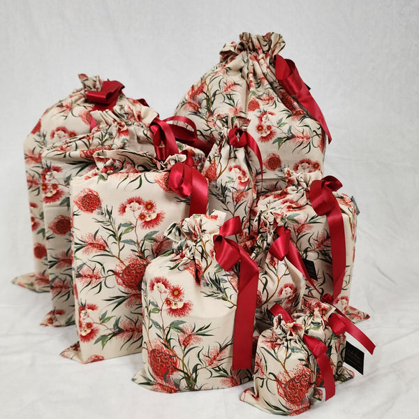 Set of ten reusable Christmas gift bags in Australiana Eucalyptus. Fabric has red and green eucalyptus flowers on a natural coloured background. The bags are tied with a red satin ribbon.
