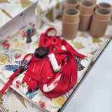 Photo showing contents of a Flora and Fauna Sew Your Own Re-Cracker (reusable Christmas crackers or bon bons) box. The fabric has kowhai, pohutukawa and tui on a white background. There is red satin ribbon, instructions, cardboard tubes, tags and thread.