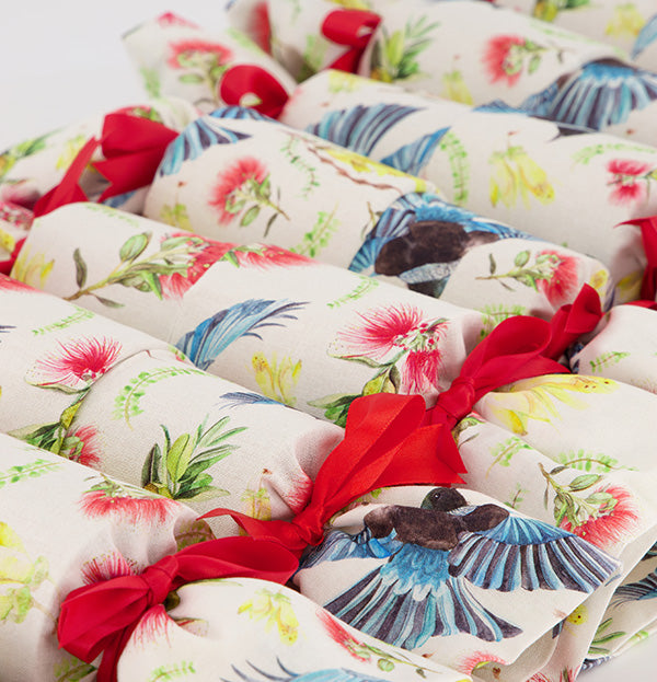 Close up of Flora and Fauna Re-Crackers (reusable eco-friendly Christmas Crackers or Bon bons). This fabric features tui, kowhai and pohutakawa on a white background. Finished with red satin ribbons.