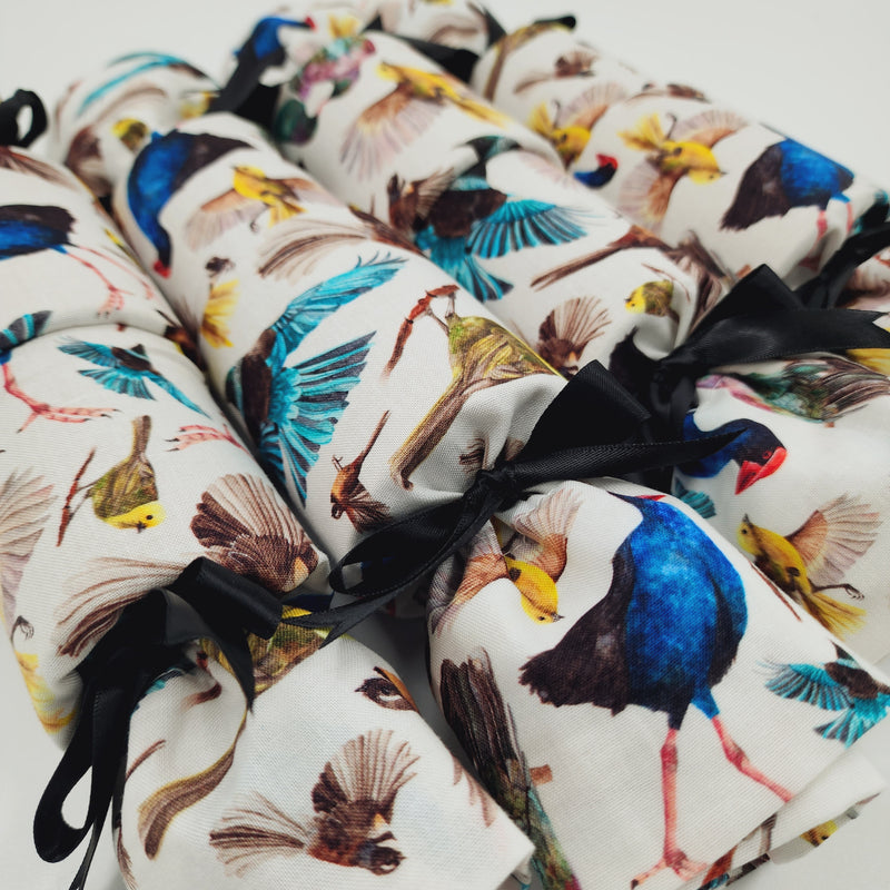 A close up of four NZ Birds Re-Crackers (reusable Christmas Crackers or Bon bons). The fabric on the crackers feature colourful native NZ birds on a white background, finished with a black satin ribbon.