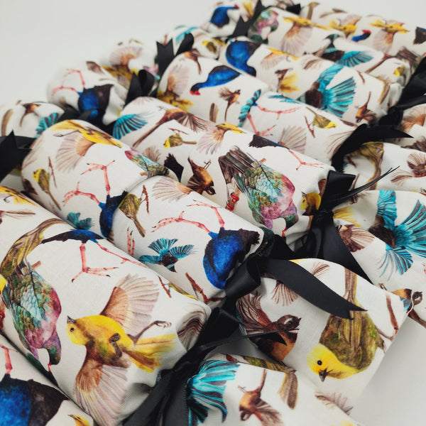 Eight NZ Birds Re-Crackers (reusable Christmas Crackers or Bon bons). The fabric on the crackers feature colourful native NZ birds on a white background, finished with a black satin ribbon.