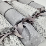 Close-up of four Silver and Ice Re-Crackers (reusable Christmas Crackers or Bon-Bons). Fabric has a sliver motif with alternating white and grey background with silver ribbon.