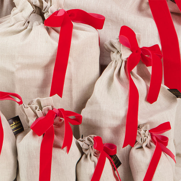 Photo shows a close up of Luxury Linen and Velvet Reusable Gift Bags. Bags are made from natural coloured flax linen, secured with a red velvet ribbon.
