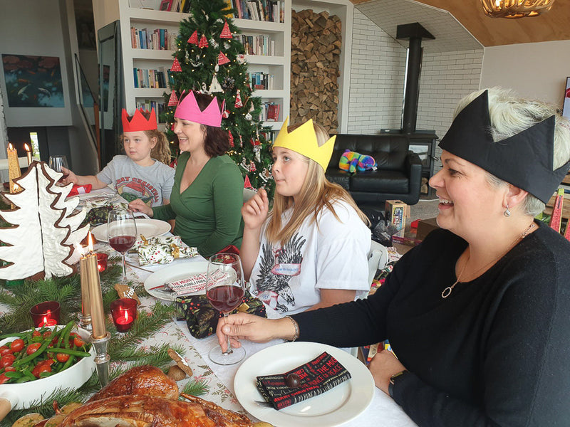 This image shows people sitting down at a table enjoying a Christmas meal. They are wearing reusable cotton crowns.